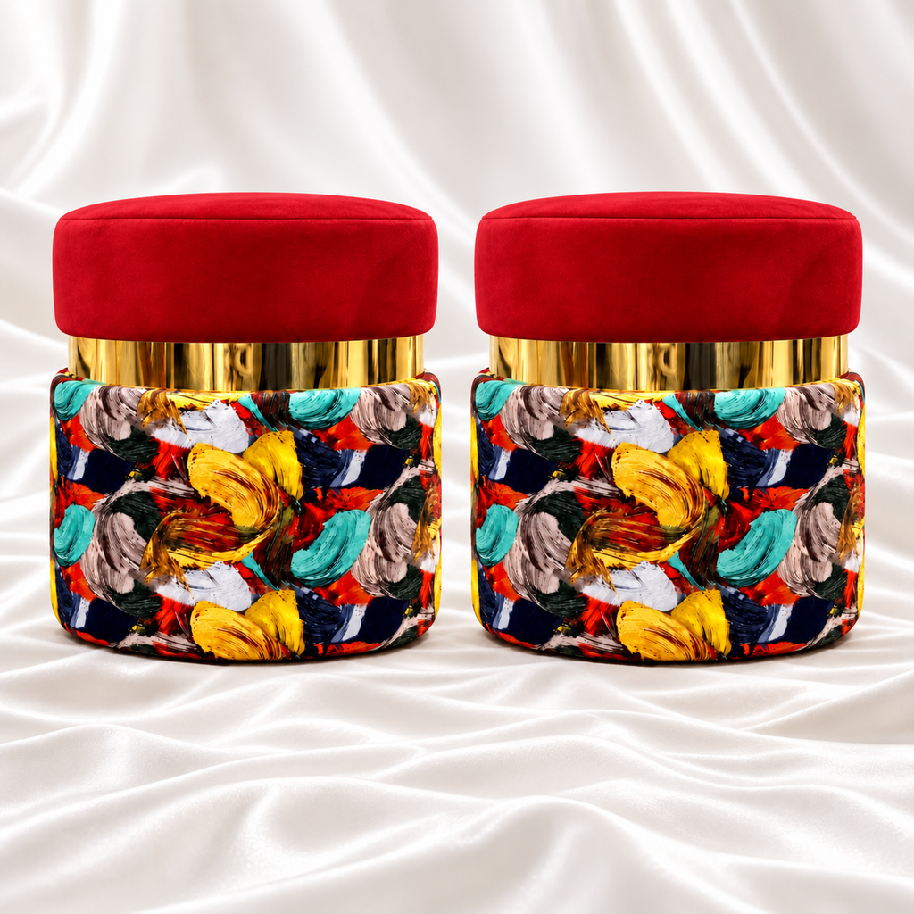 Pair of round ottoman stools with red velvet seats, reflective gold bands and multicoloured abstract upholstery on white satin fabric.