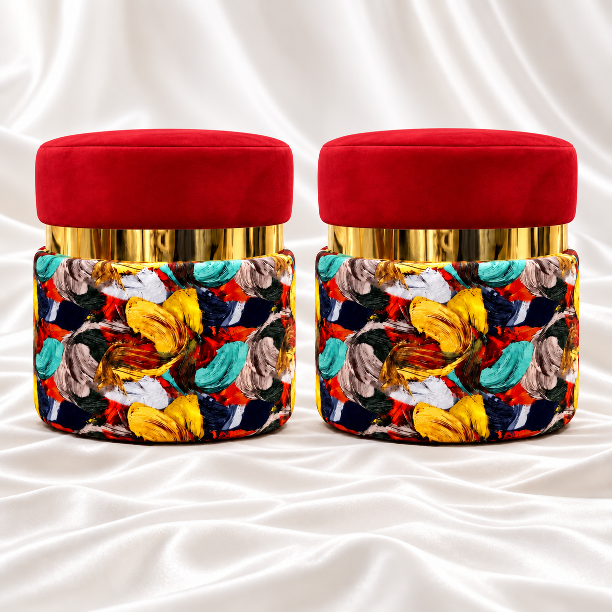 Pair of round ottoman stools with red velvet seats, reflective gold bands and multicoloured abstract upholstery on white satin fabric.