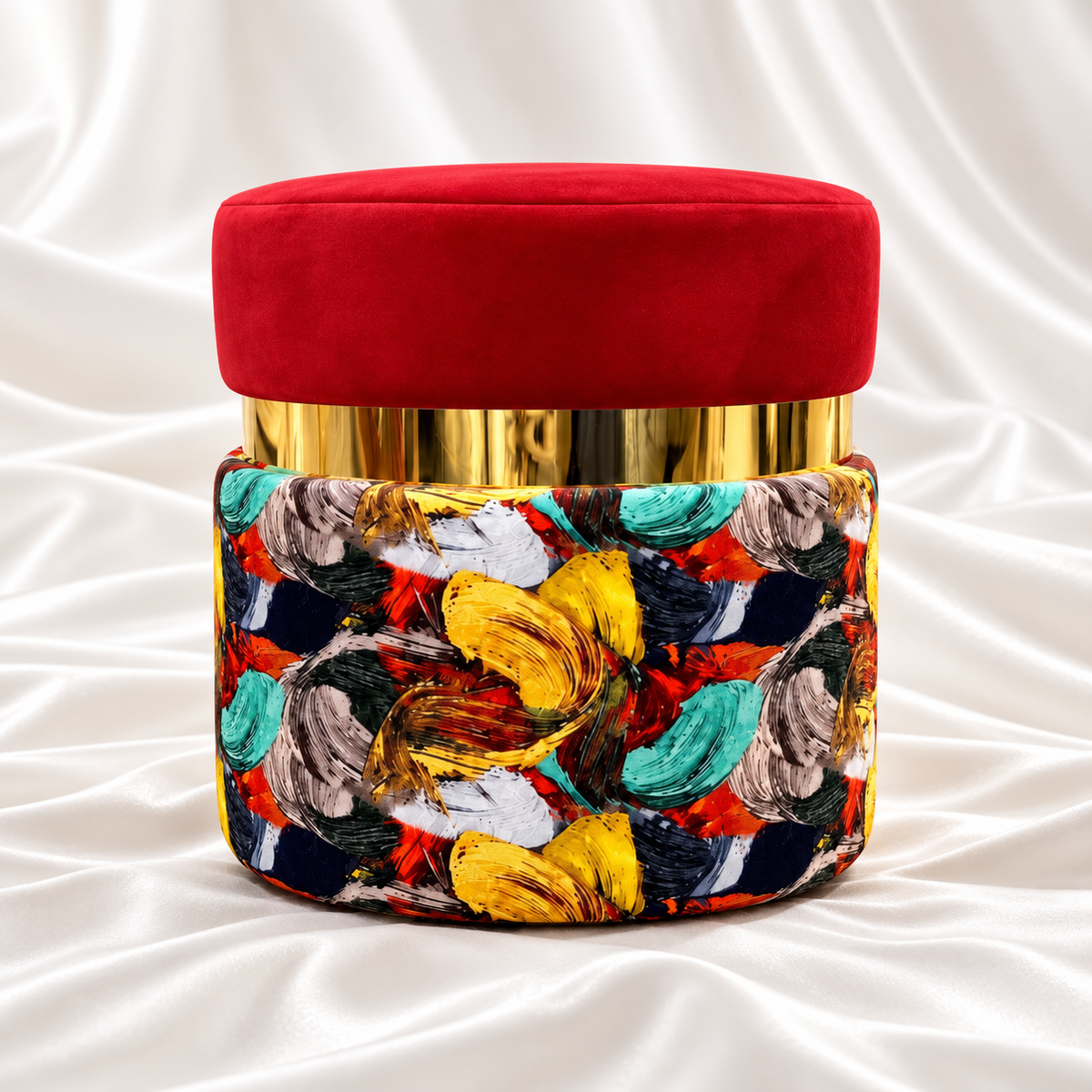 Single round ottoman stool with a red velvet seat, reflective gold band and multicoloured abstract upholstery on white satin fabric.