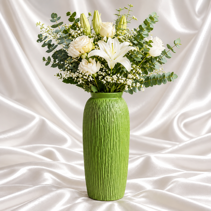 12-inch apple green decorative vase with vertical bark texture, styled with white lilies, roses and eucalyptus against draped white satin fabric.