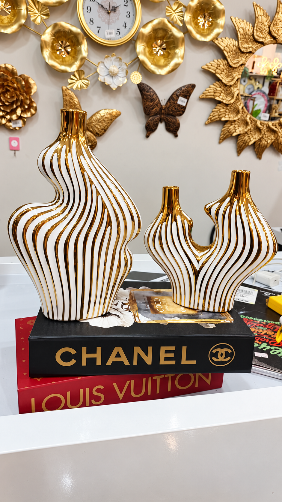Set of two sculptural white vases with gold wave stripes displayed against a decorative shop background