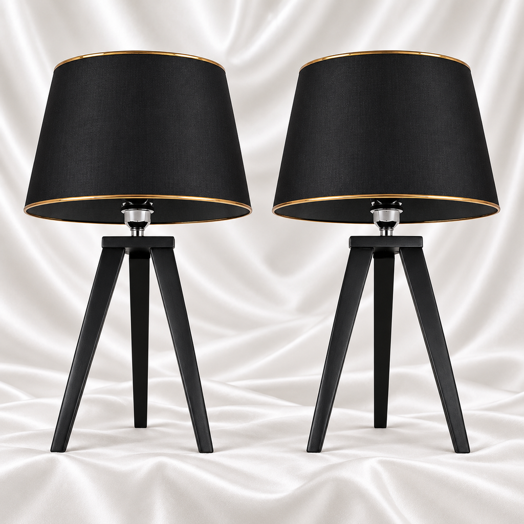 Pair of black tripod table lamps with black tapered shades and gold-tone trim, displayed against a white satin fabric background.