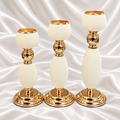 Three ivory spiral-ribbed candle holders in graduated heights with gold-tone rims, stems and round bases, displayed on white satin fabric.