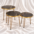 Set of three round black marble-effect side tables with gold-tone rims and slender hairpin legs on a white satin fabric background.
