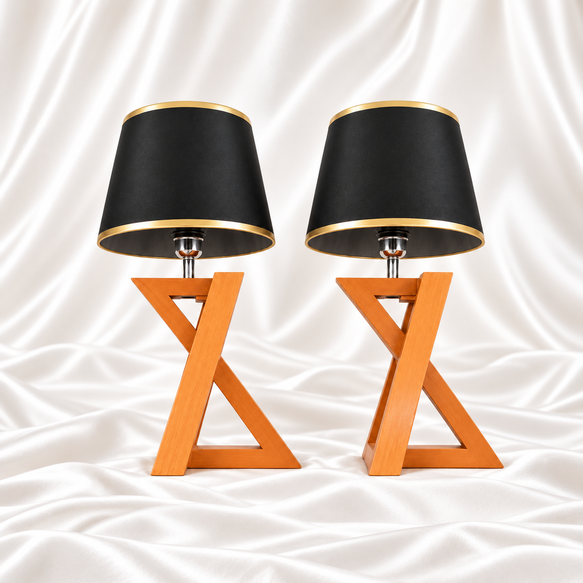 Pair of matching table lamps with black and gold-trimmed shades and wooden X-frame bases on white satin fabric.
