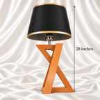 Single 28-inch table lamp with a black and gold-trimmed shade and wooden X-frame base on white satin fabric.