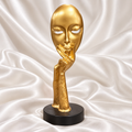 Gold abstract face sculpture with hand-under-chin design and black circular base, displayed on white satin with the Decoreway logo.