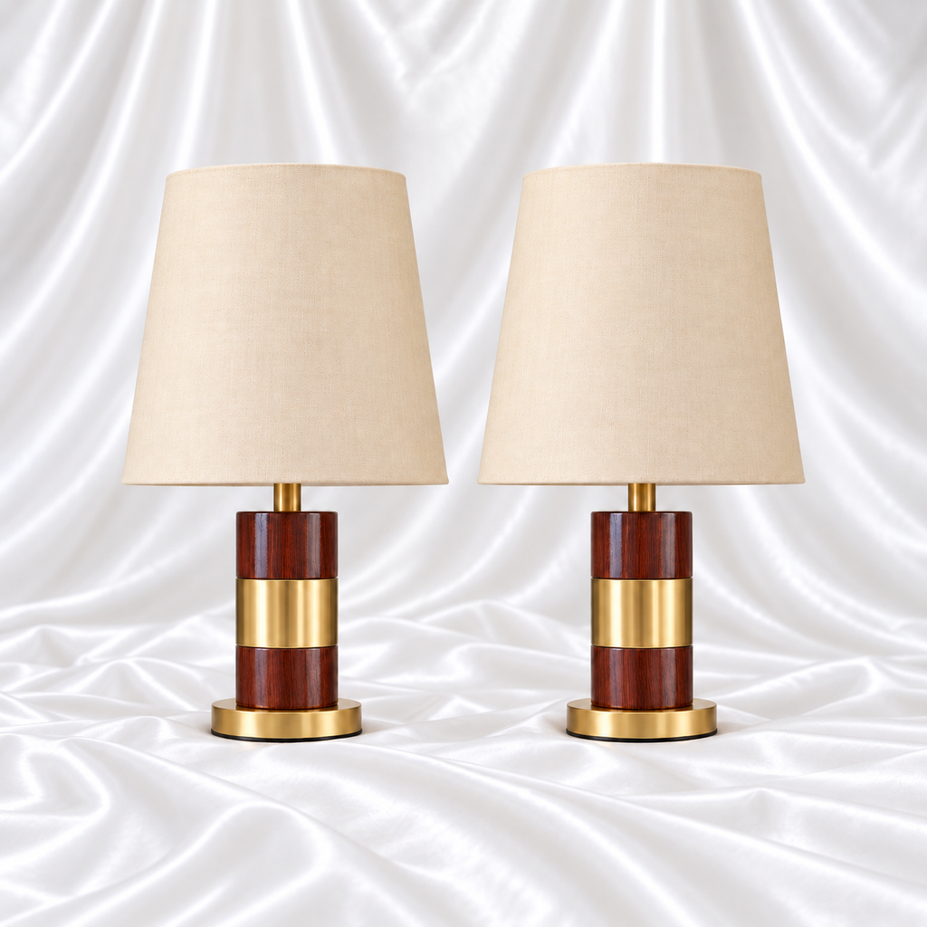 Pair of brown woodgrain-look table lamps with wide gold-tone centre bands, round gold bases and plain cream tapered shades on white satin fabric.