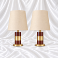 Pair of brown woodgrain-look table lamps with wide gold-tone centre bands, round gold bases and plain cream tapered shades on white satin fabric.
