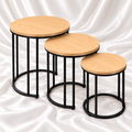 Three honey blonde round nesting tables with light woodgrain-effect tops and black metal frames on white satin fabric.