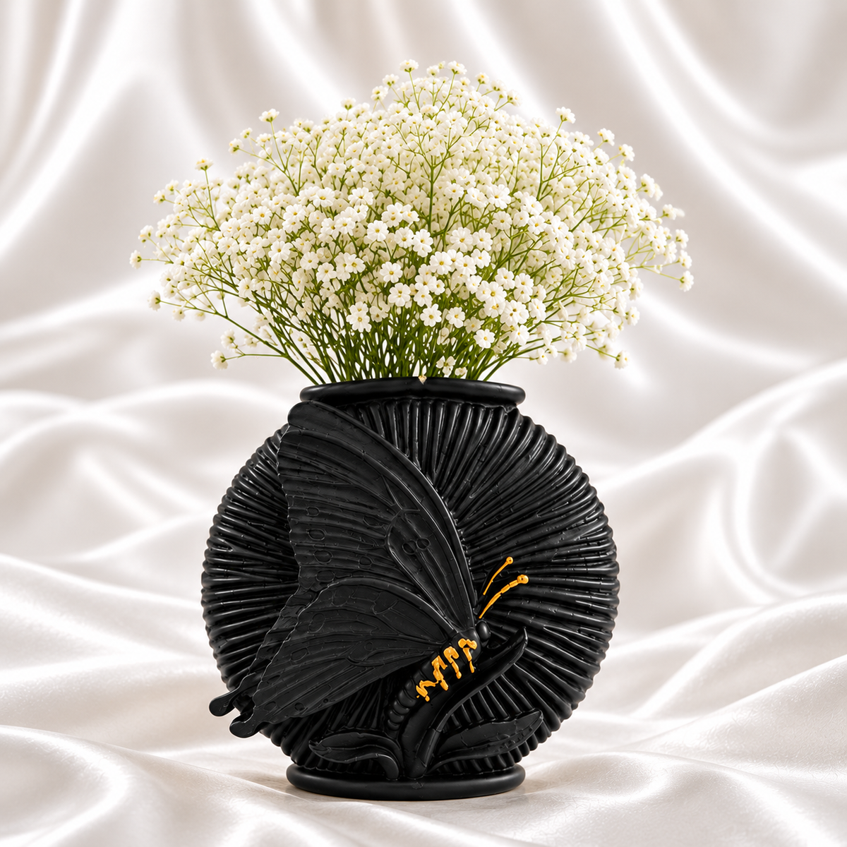 Black ribbed butterfly vase with small gold accents and white flowers on a white satin background.