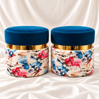 Pair of luxury blue velvet floral ottoman stools featuring colourful floral upholstery and gold-tone accents on white satin fabric.