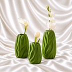 Set of three leaf green decorative vases in graduated sizes with raised leaf patterns and white flowers, displayed on white satin fabric.