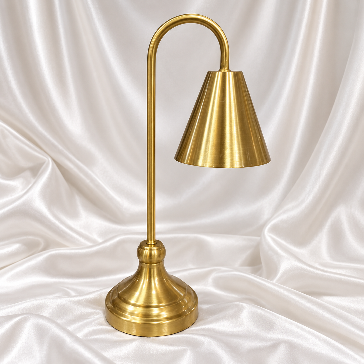 Luxury golden table lamp with elegant cone shade and curved stand on white satin background.