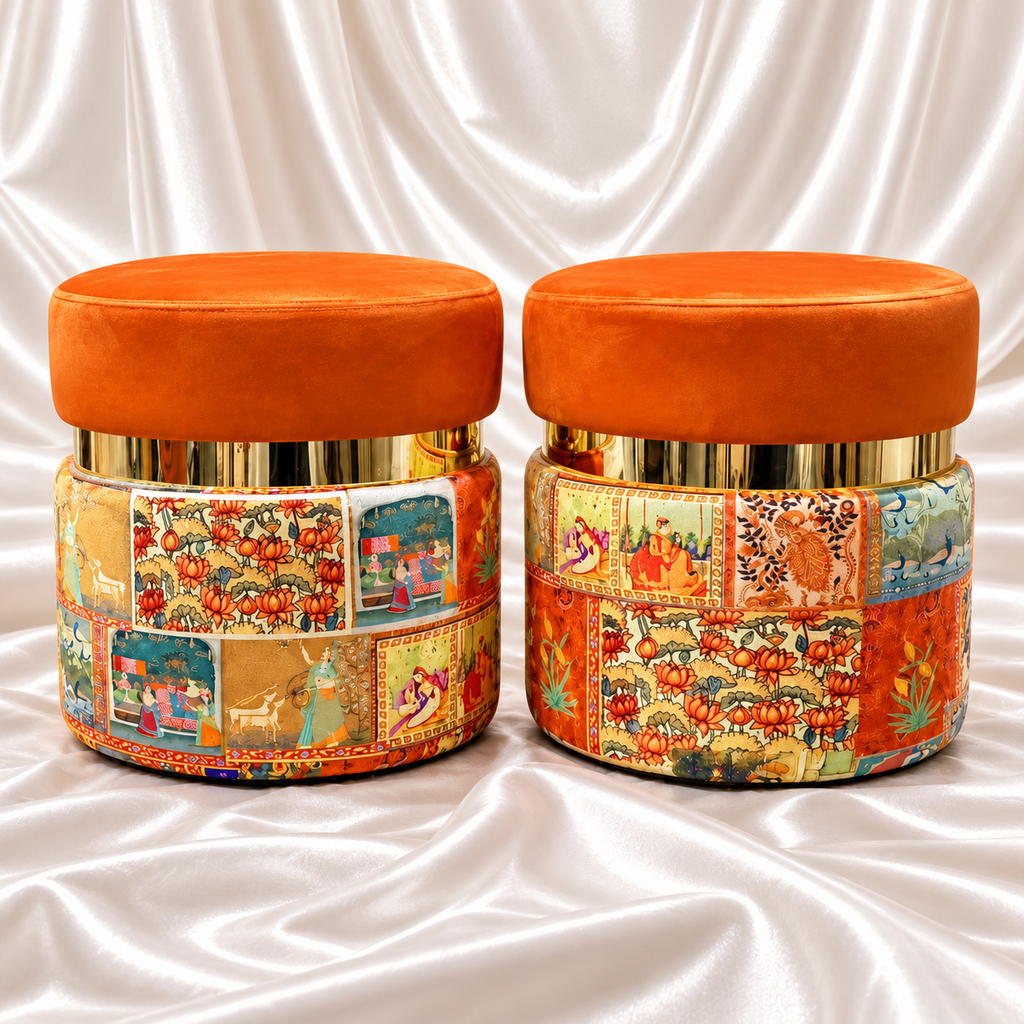 Pair of orange ottoman stools with gold-tone bands and multicolour patchwork bases on white satin fabric.