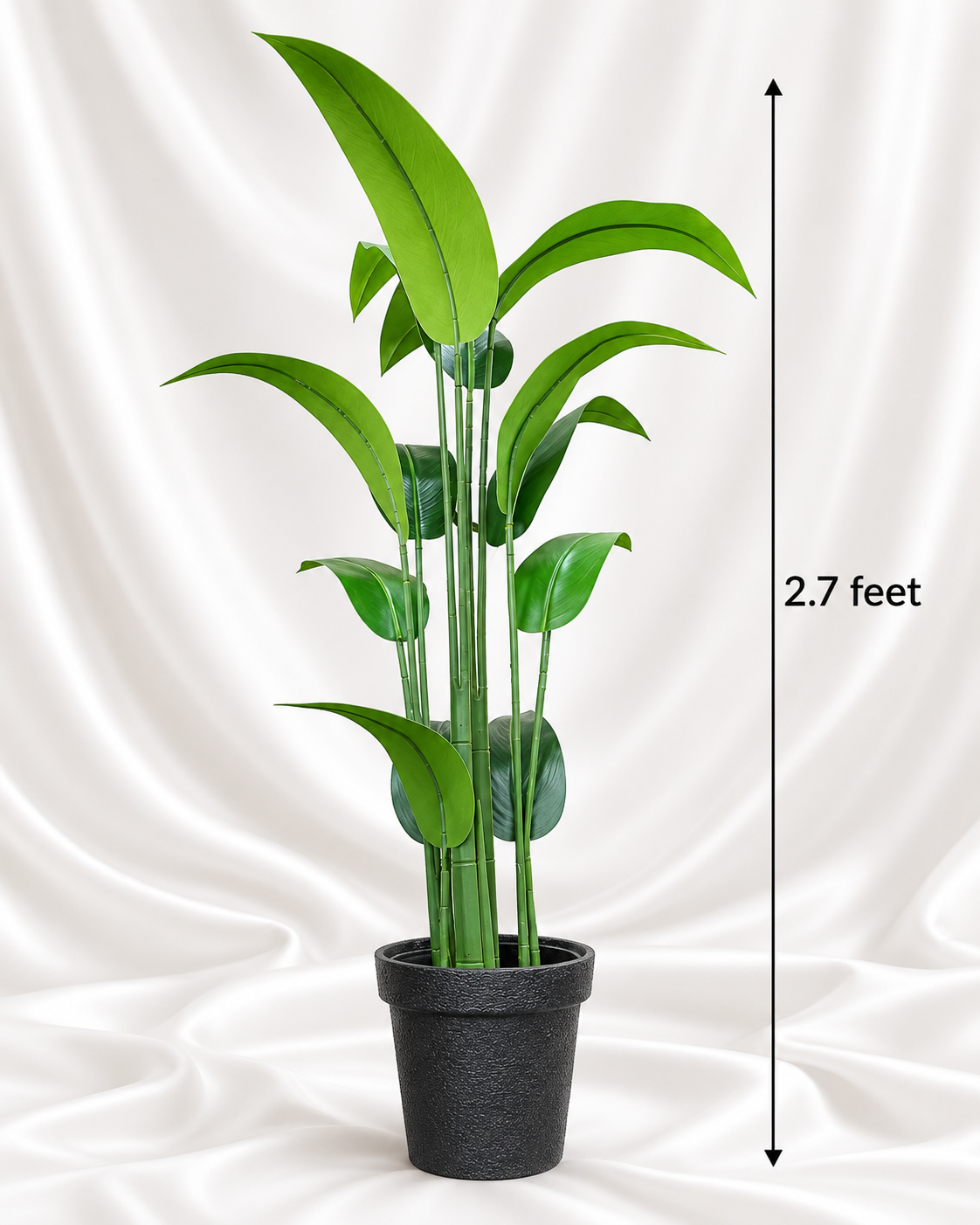 Imported artificial green plant with tall slender leaves in a dark textured pot, shown against white satin fabric with a 2.7-foot height line.