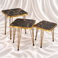 Three square black marble-effect side tables in graduated heights with gold-tone rims and hairpin legs on a white satin background.