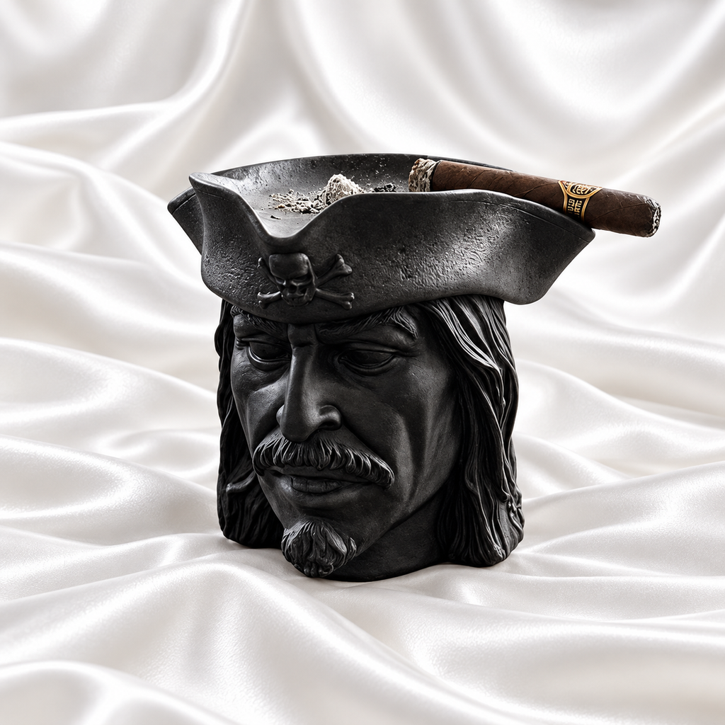 Black pirate head ashtray with textured hair and a matching skull-and-crossbones hat, holding a cigar on white satin fabric.