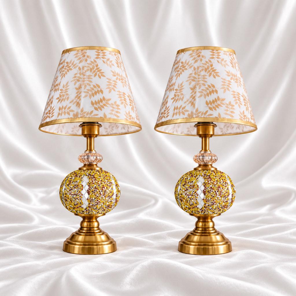 Pair of gold mosaic table lamps with reflective diamond accents, gold-tone bases and white shades with beige-gold leaf patterns on white satin fabric.