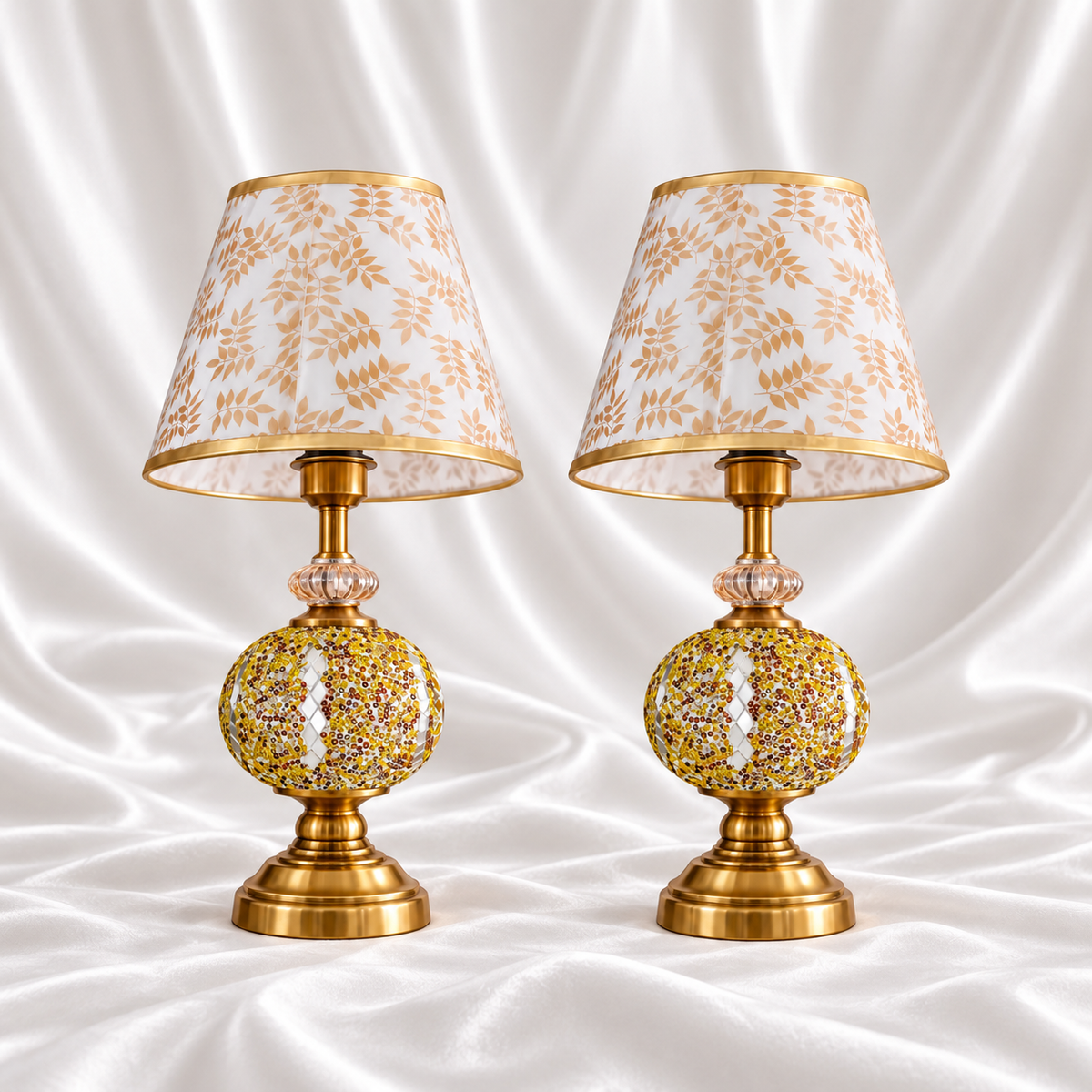 Pair of gold mosaic table lamps with reflective diamond accents, gold-tone bases and white shades with beige-gold leaf patterns on white satin fabric.