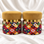 Set of 2 luxury mustard gold velvet ottoman stools with gold accents and colourful geometric fabric upholstery on white satin background.