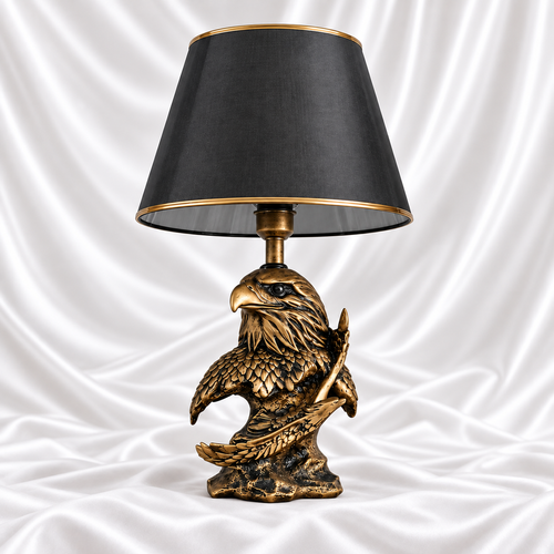 Single antique gold and black eagle table lamp with a tapered black shade and gold trim, displayed on white satin fabric.