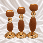 Three brown spiral-ribbed candle holders in graduated heights with gold-tone rims, stems and round bases, displayed on white satin fabric.