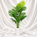 Artificial palm plant with green fronds in a white textured pot against a white satin fabric background.