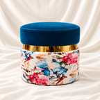 Luxury blue velvet floral round ottoman stool with gold-tone accent by Decoreway, displayed on a soft white satin fabric background.